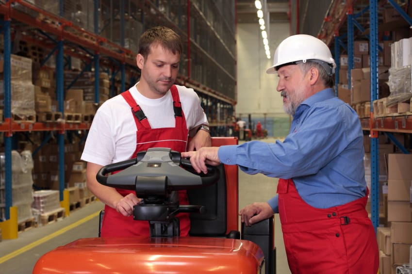 A senior worker teaching his junior the operation of a fork lift vehicle in a factory