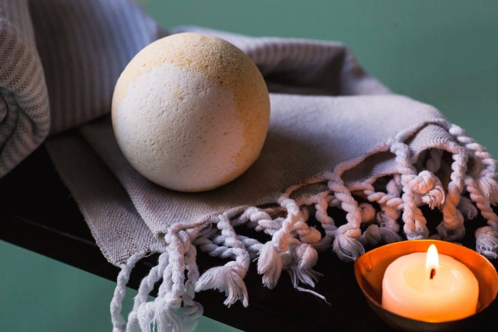 A bath bomb resting and towel with a candle