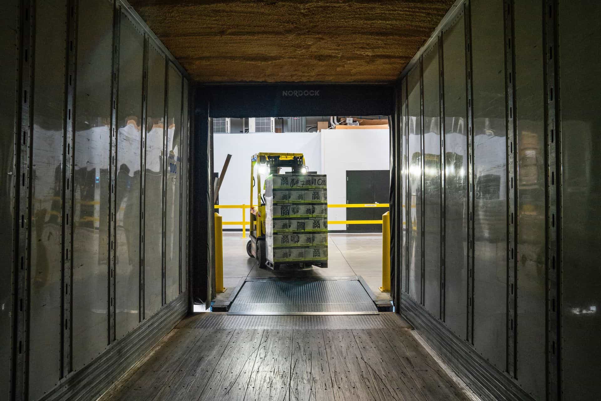 Shrink wrapped pallet being carried off a lorry by a forklift