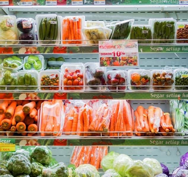 A supermarket fridge filled with plastic-wrapped vegetables